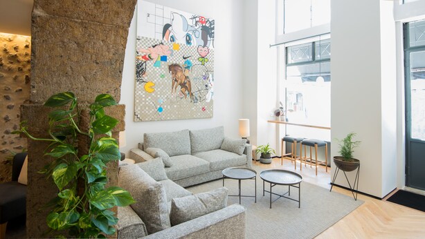 A modern living room with a grey sofa, two small round tables, and a large abstract painting on the wall. - Urbano FLH Hotels Lisboa (Lisbon)