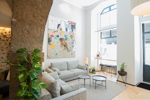 Ein modernes Wohnzimmer mit einem grauen Sofa, zwei kleinen runden Tischen und einem großen abstrakten Gemälde an der Wand.