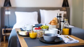 A neatly arranged breakfast tray on a bed with a pillow, a bedside table with a lamp, and a bottle of orange juice. - Urbano FLH Hotels Lisboa (Lisbon)