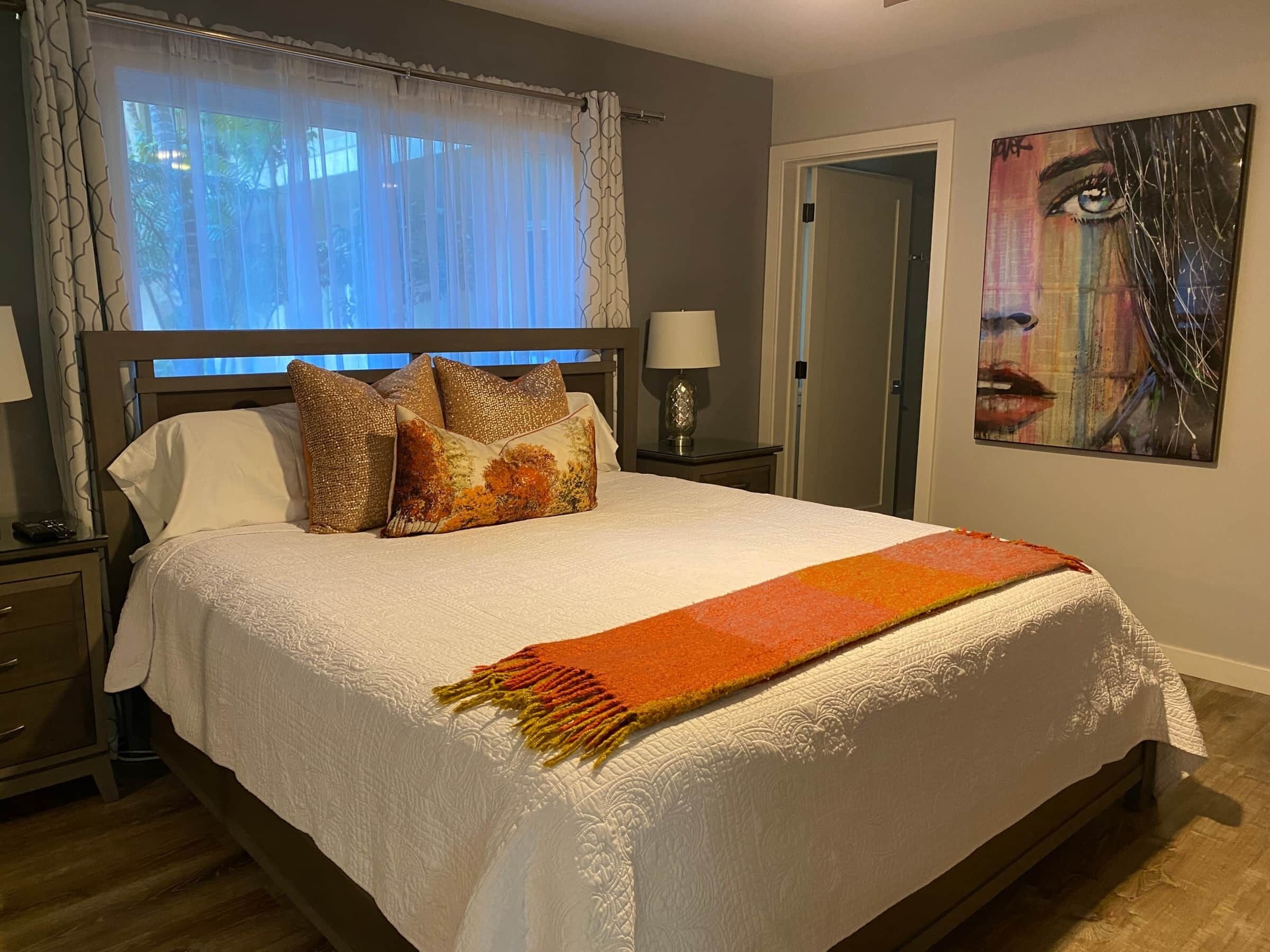 Una cama bien hecha con edredón blanco, una manta estampada y almohadones decorativos.
