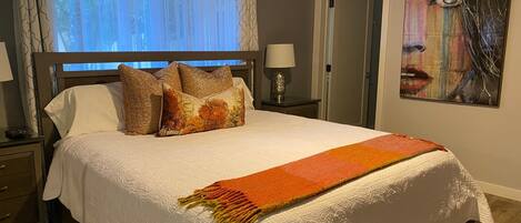 Una cama bien hecha con edredón blanco, una manta estampada y almohadones decorativos.