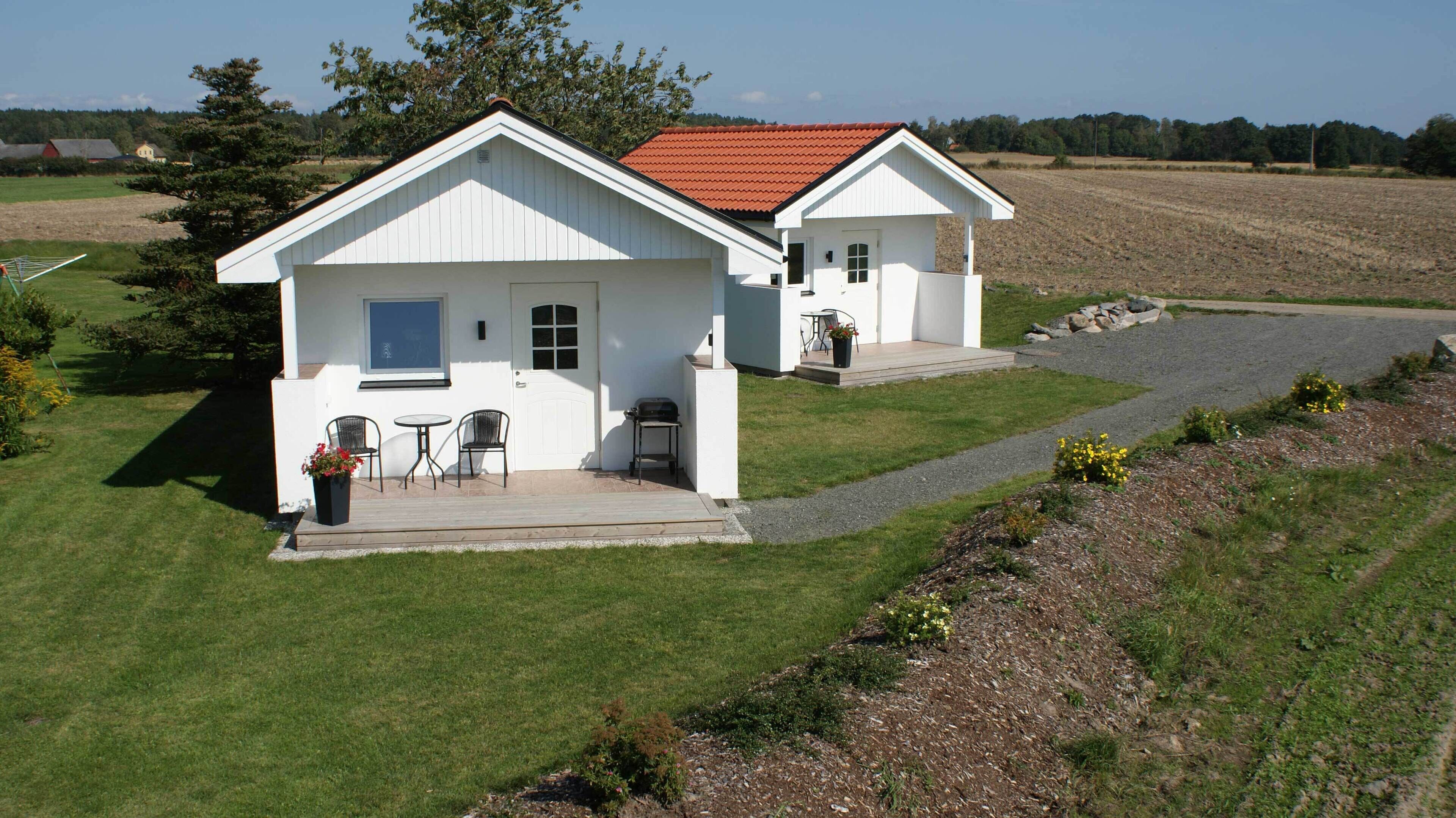 A white two-story house with a red roof, a front porch with a table and chairs, and a small garden area.