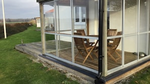 A glass-enclosed patio with a wooden deck, outdoor furniture, and a view of the surrounding landscape. - Nordanå Gård (Vinslov)