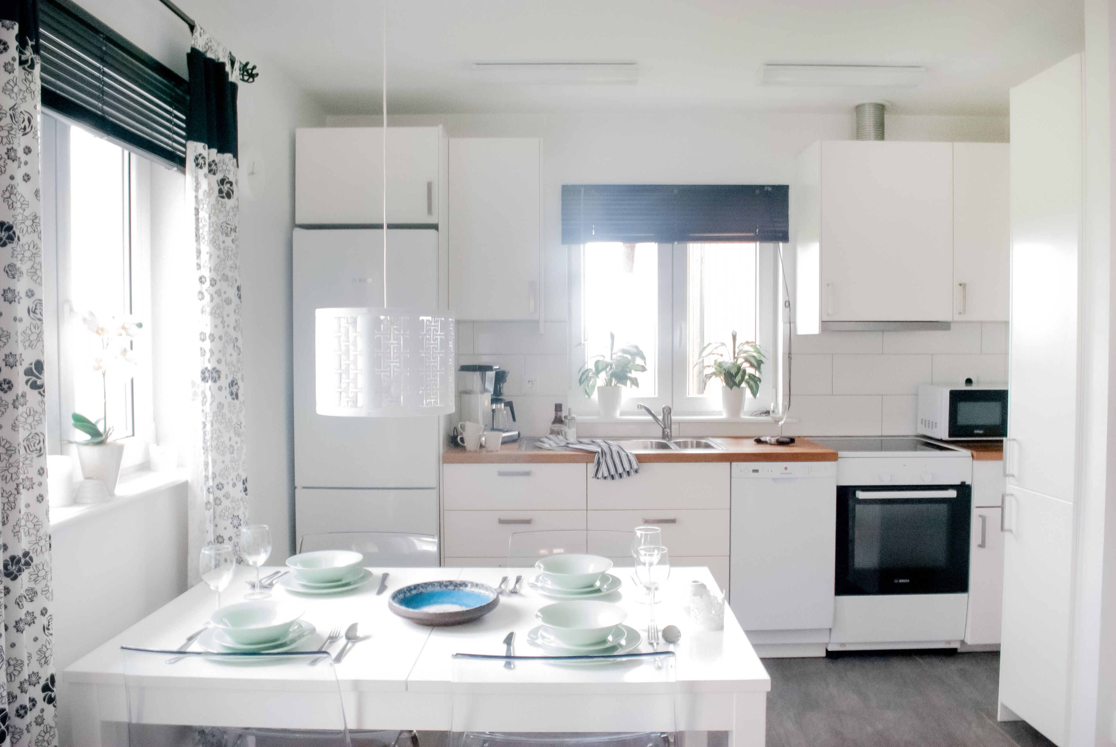 Una cocina moderna con armarios blancos, una mesa de comedor con platos y cubiertos, un microondas y un lavavajillas.