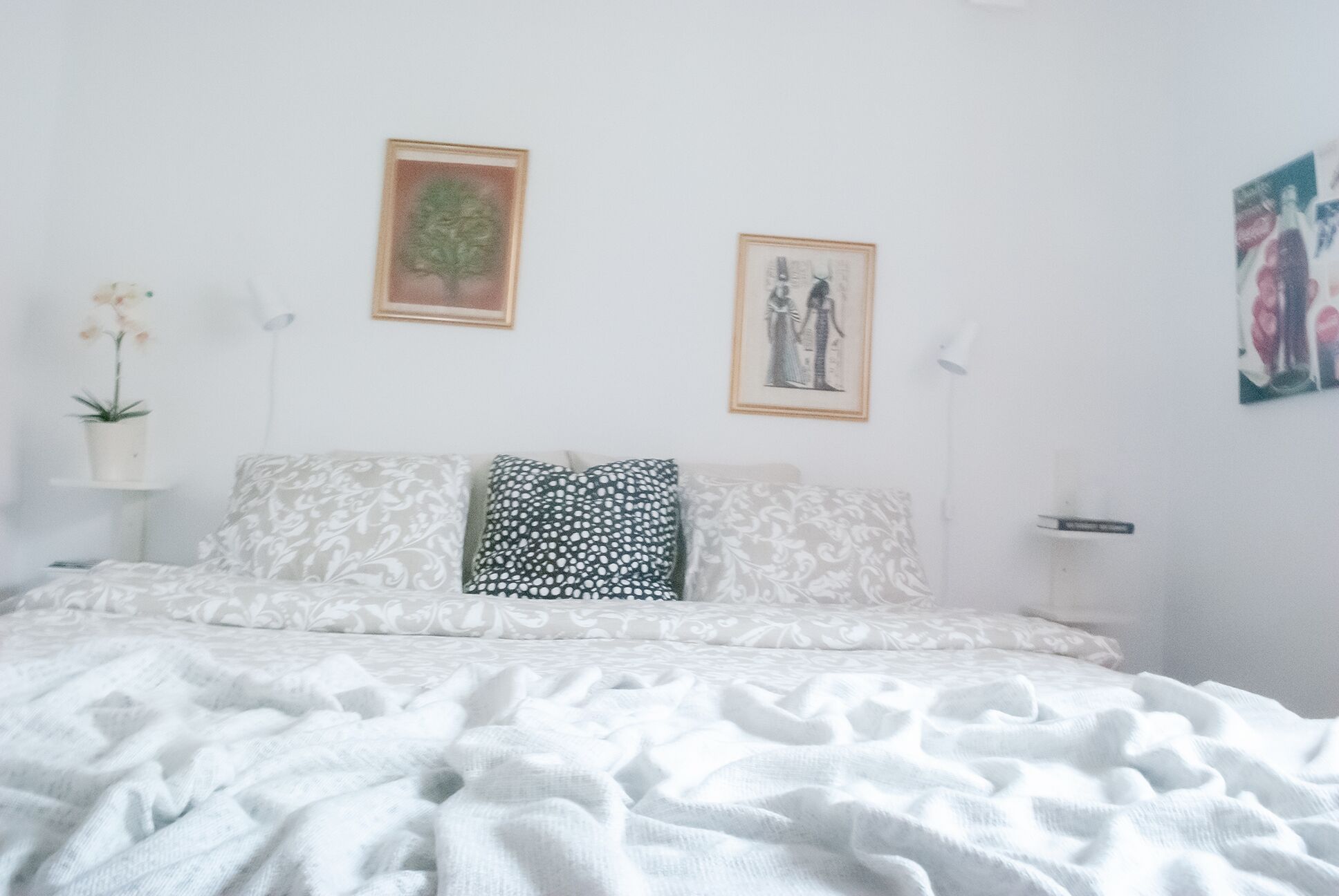 A bedroom with a bed, two pillows, a nightstand, a lamp, and wall art.