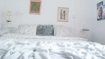 A bedroom with a bed, two pillows, a nightstand, a lamp, and wall art.