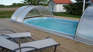 A swimming pool with a glass enclosure, surrounded by a wooden deck and equipped with lounge chairs. - Nordanå Gård (Vinslov)