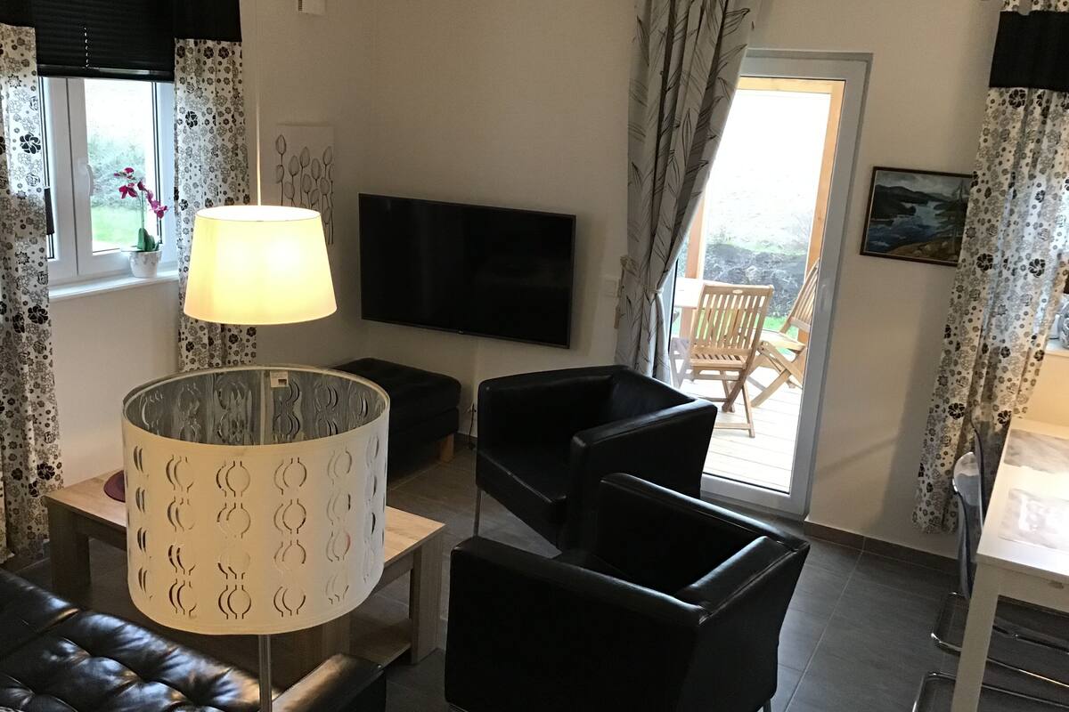 Una sala de estar con sofá, sillas, televisor, lámpara y ventana con cortinas.