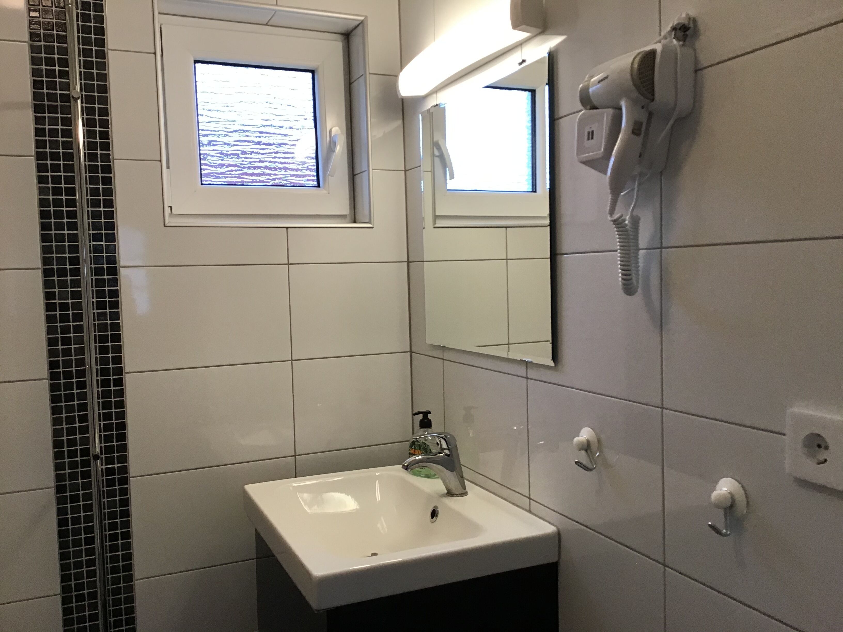 Une salle de bain avec un lavabo blanc, un miroir, un sèche-cheveux et une fenêtre donnant sur la mer.