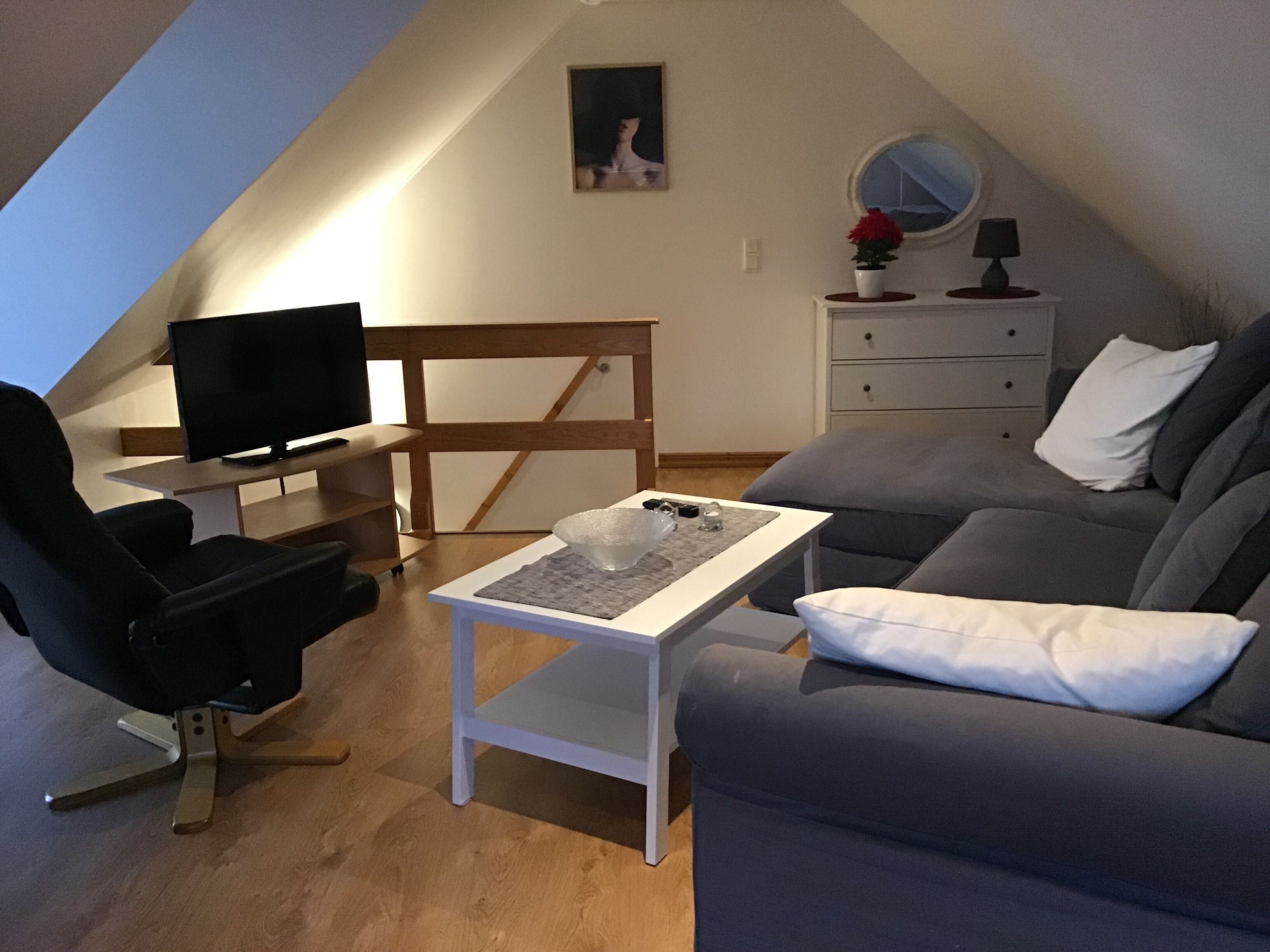 Ett sovrum på vinden med en tv, en soffa, ett litet bord och en byrå.