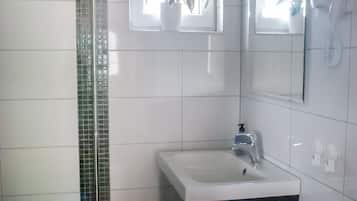 Un baño con lavamanos blanco, espejo, secador de pelo y planta en maceta.