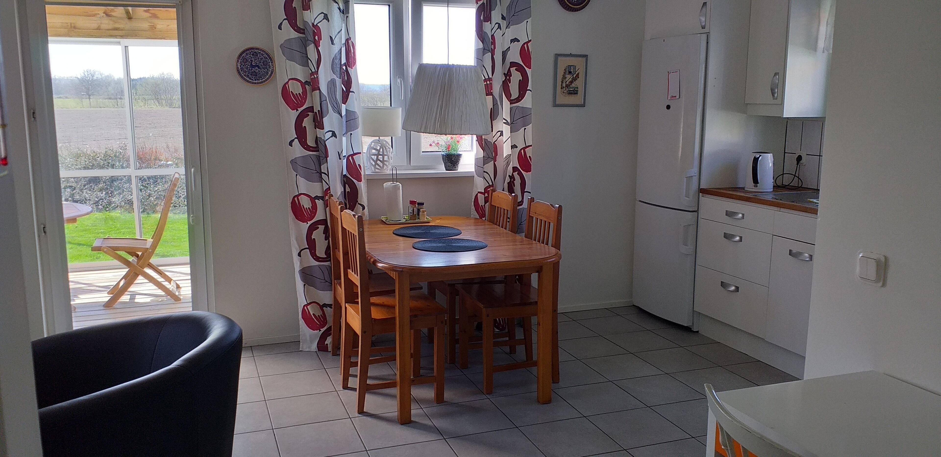 A dining area with a table and chairs, a kitchen with cabinets and appliances, and a view of the outdoors through a door.