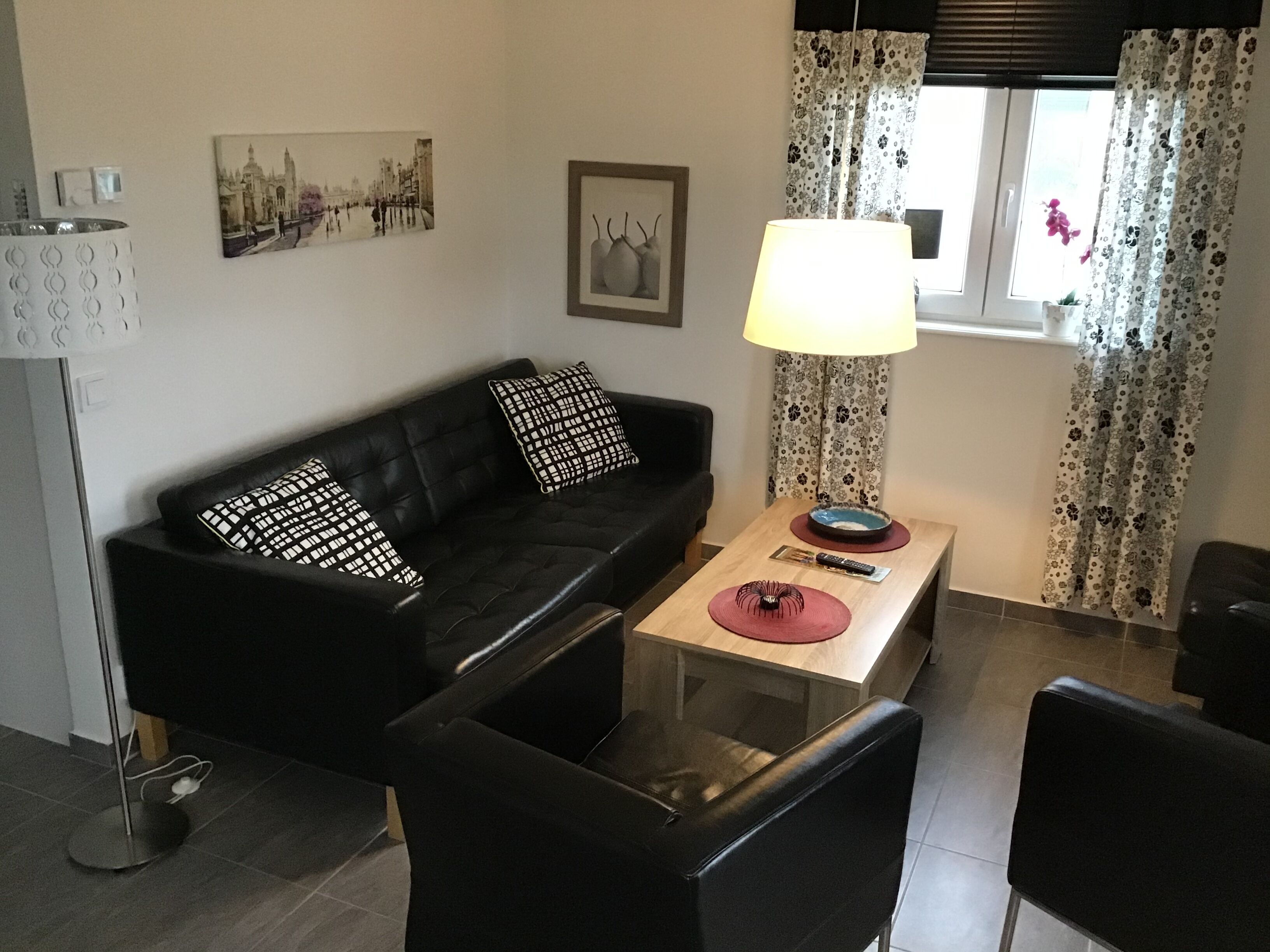 Una sala de estar moderna con un sofá negro, una mesa de centro de vidrio, una lámpara y un cuadro en la pared.