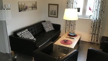 A modern living room with a black sofa, a glass coffee table, a lamp, and a painting on the wall.