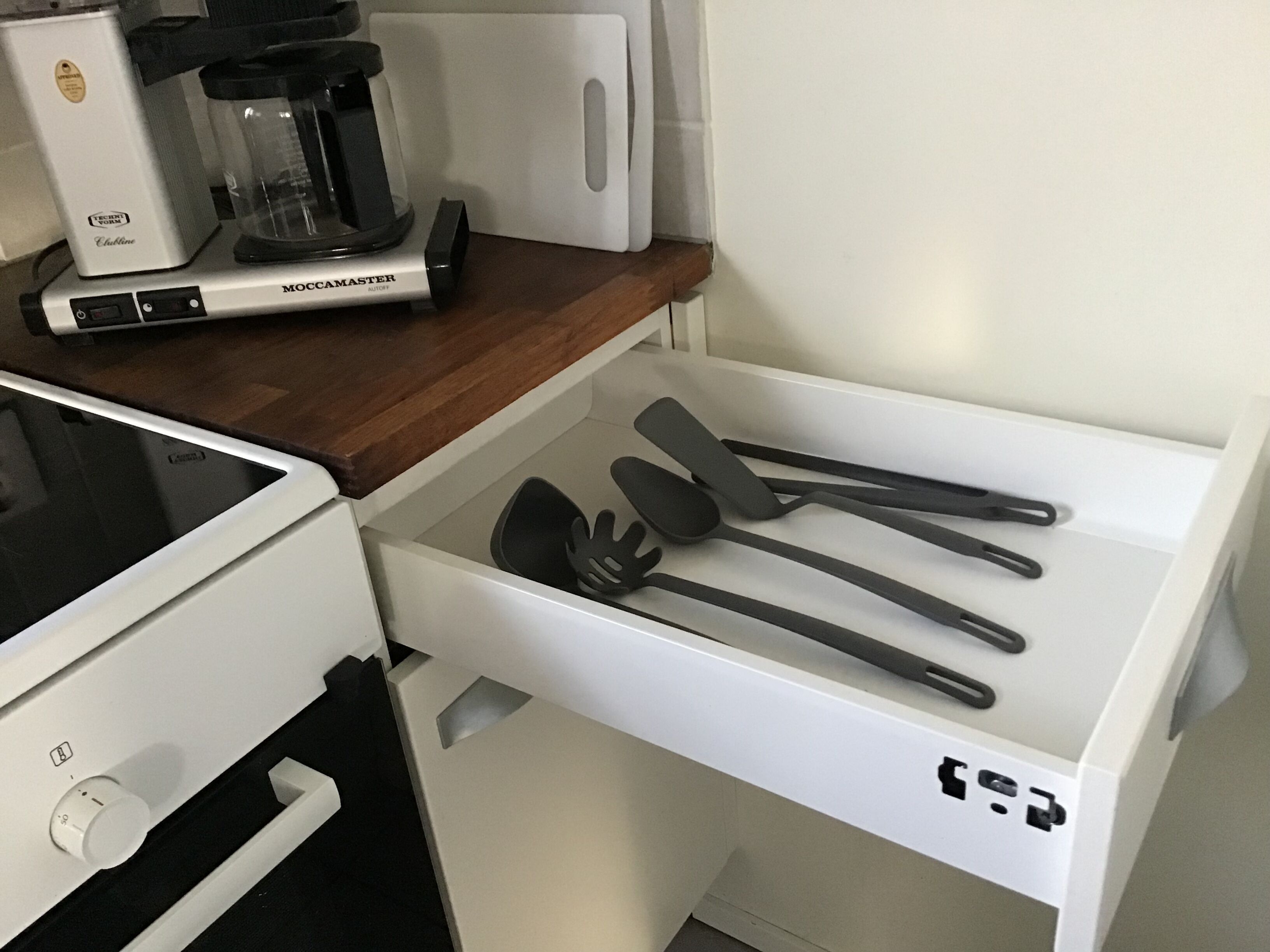 Keittiössä on valkoinen työtaso, kahvinkeitin ja laatikko, jossa on keittiövälineitä.
