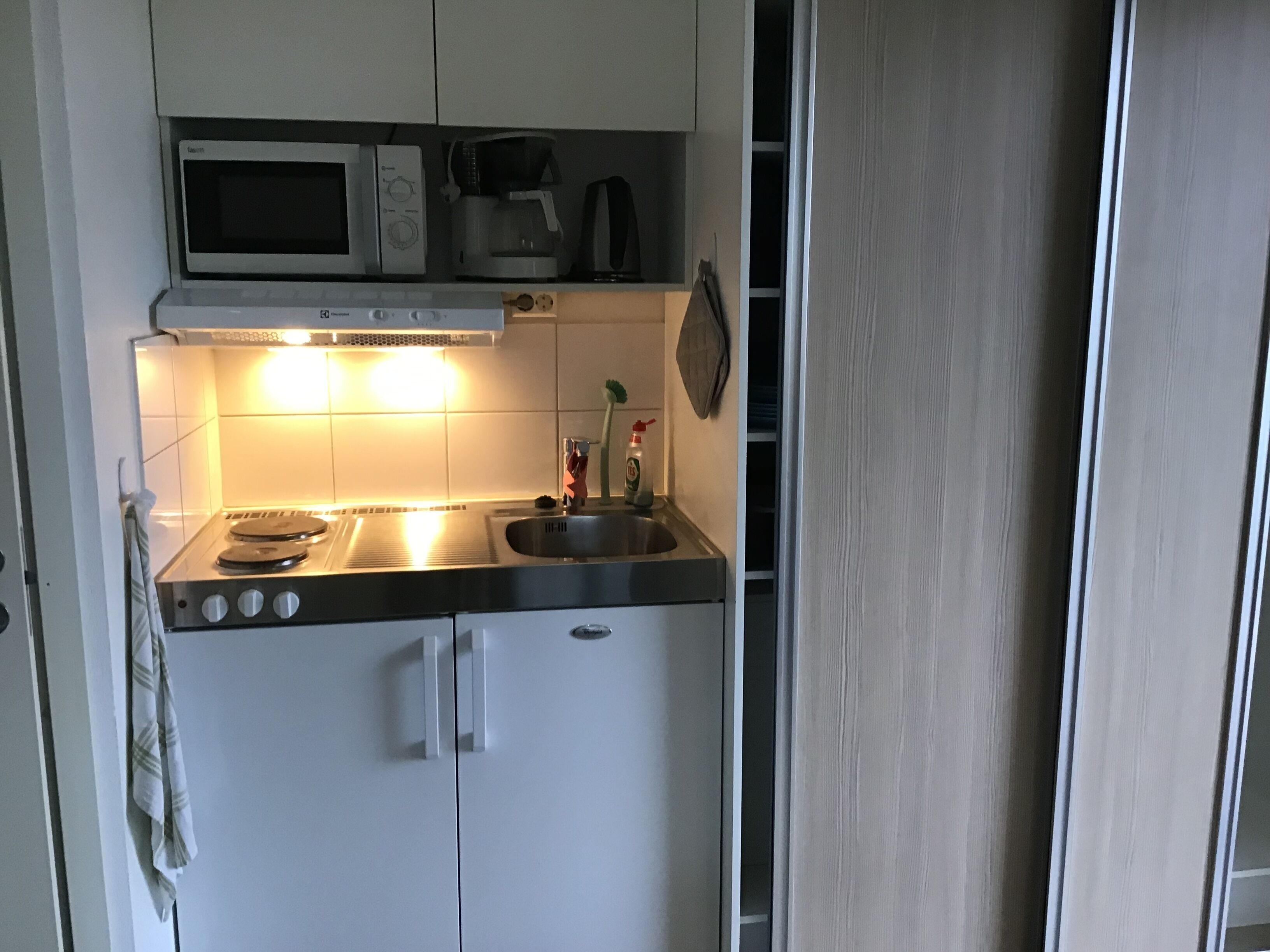 Cocina compacta con microondas, cafetera y lavamanos.