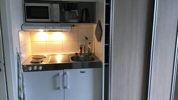 Cocina compacta con microondas, cafetera y lavamanos.