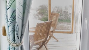 A wooden deck with a chair, a curtain with leaf patterns, and a view of trees through a glass door. - Nordanå Gård (Vinslov)