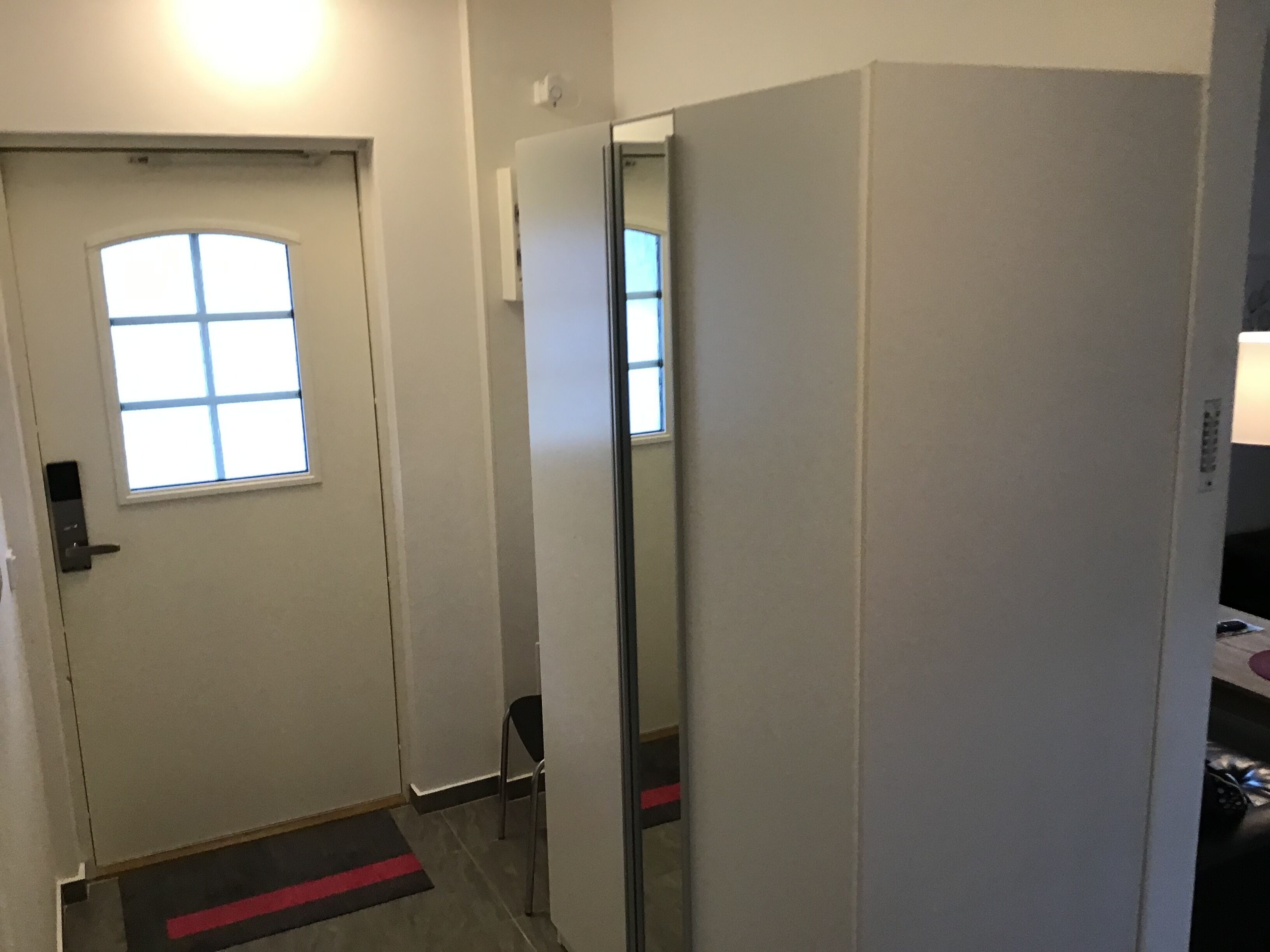 Un couloir avec une porte, une fenêtre, une chaise et un miroir.