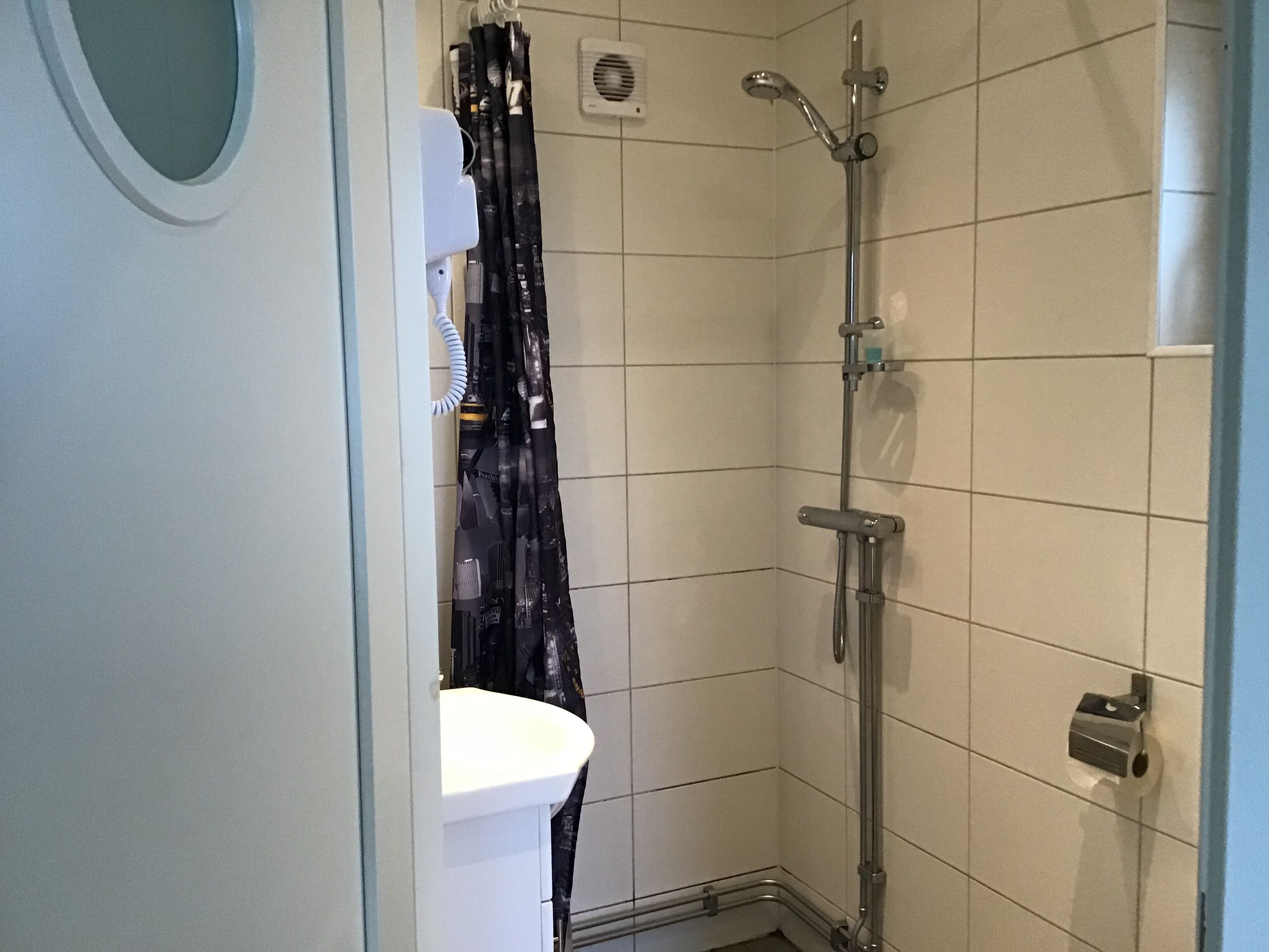 A small, tiled bathroom with a shower, a white sink, and a towel rack.