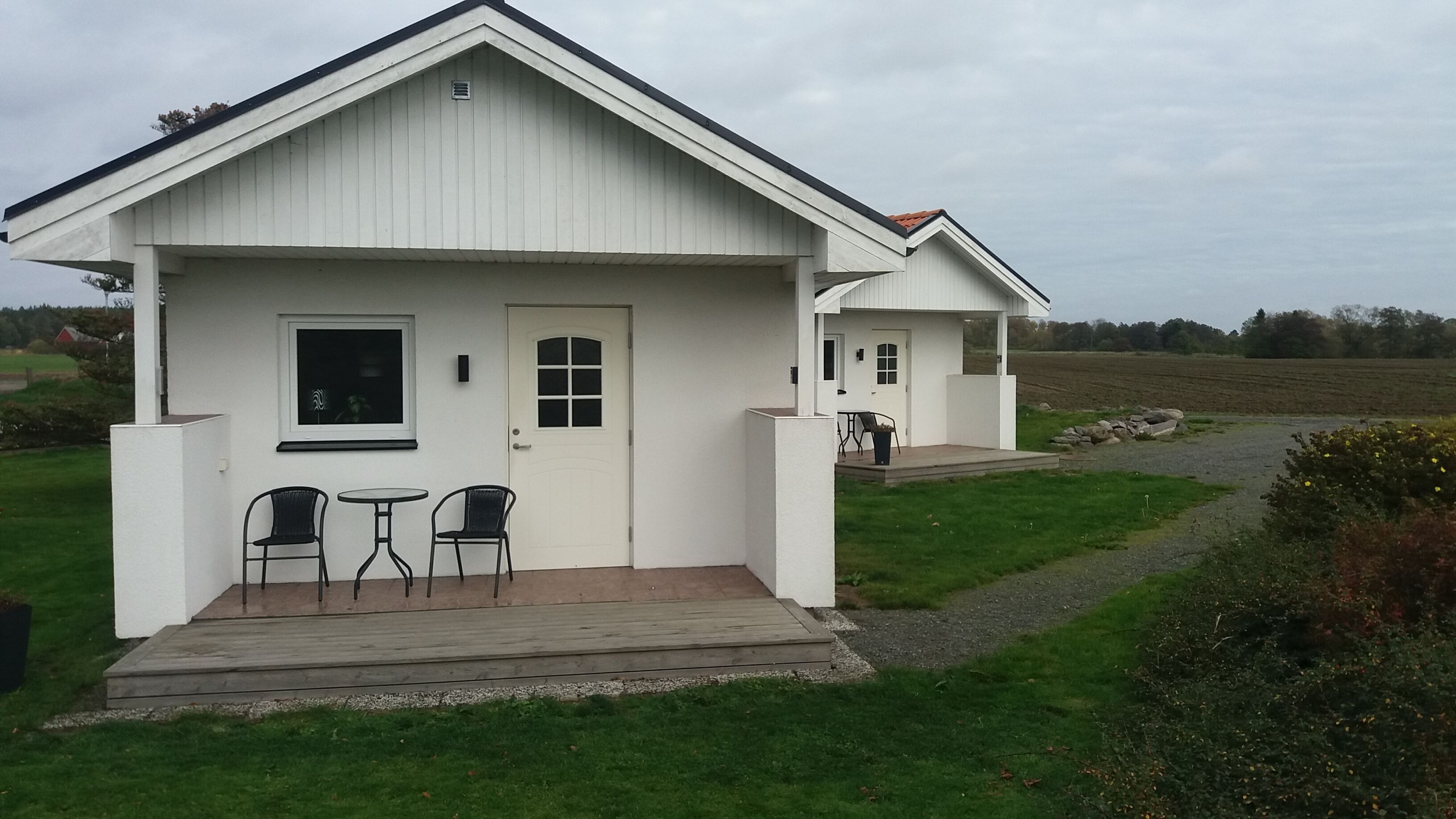 Ett vitt hus i två våningar med en veranda, ett litet bord och två stolar.