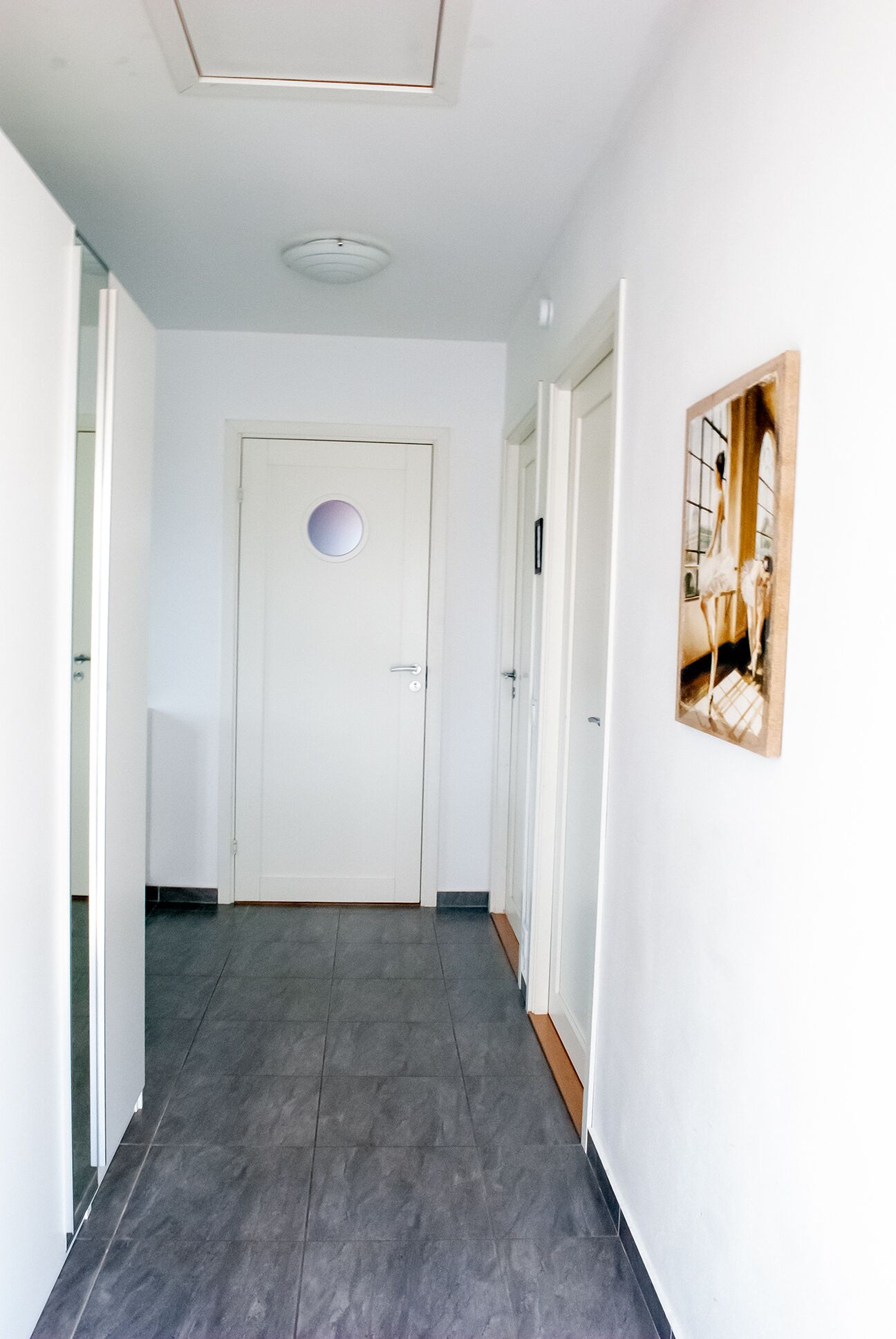 En hall med en vit dörr, en inramad tavla på väggen och en taklampa.