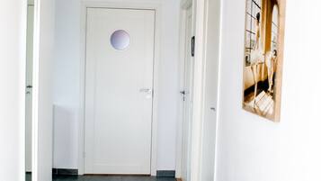 En hall med en vit dörr, en inramad tavla på väggen och en taklampa.