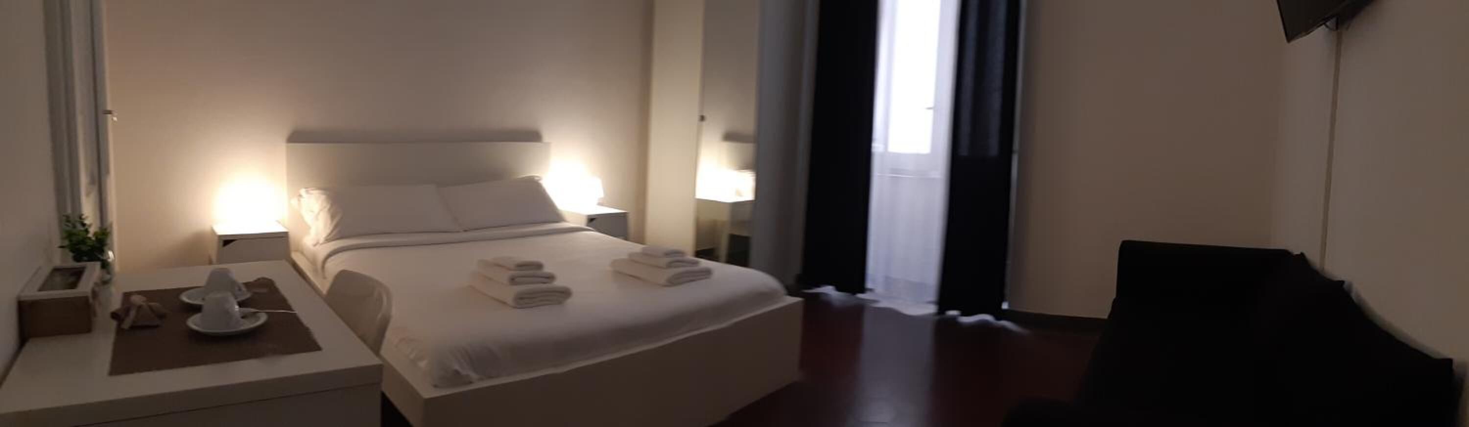 A hotel room with a bed, bedside lamps, a desk with a chair, and a view of the outdoors.