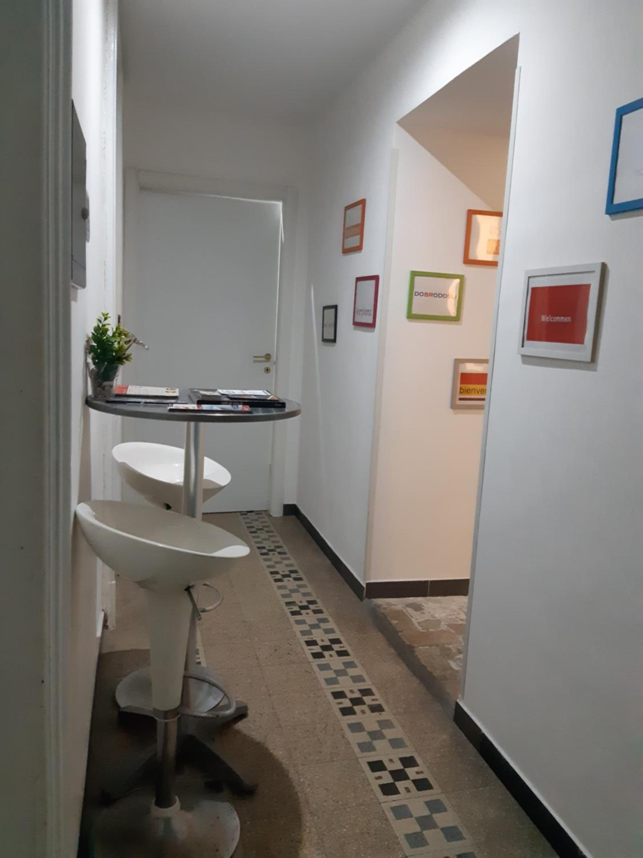 A narrow hallway with a white door at the end, a small table with chairs, and a tiled floor.