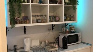 Cocina con armarios blancos, un lavamanos y un microondas. Hay estantes sobre el lavamanos con varios objetos, incluyendo un letrero que dice 'What you love'.