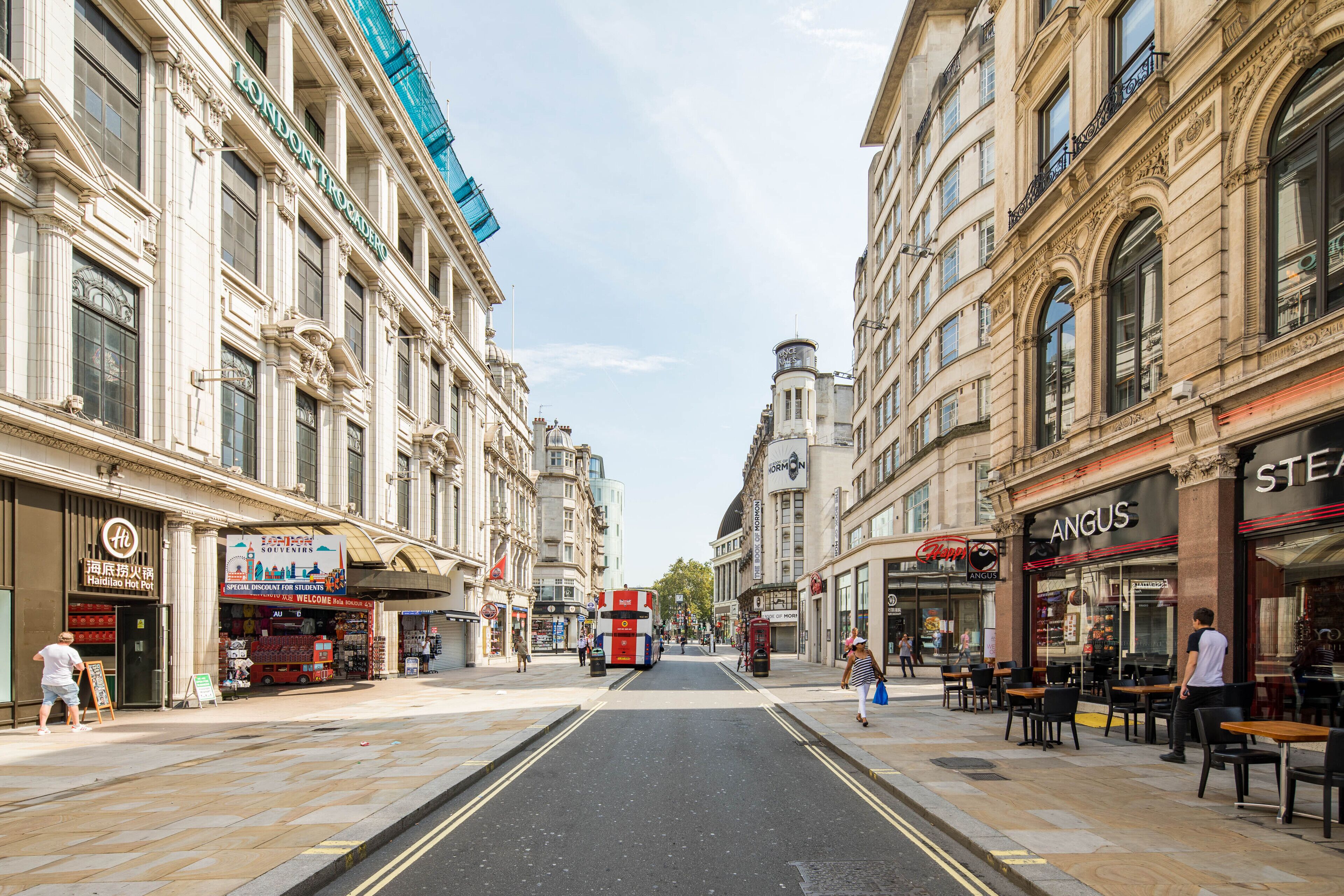 A street view with a double-decker bus, shops, and outdoor seating areas.