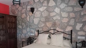 Un dormitorio con pared de piedra, un armario de madera, una cama con estructura metálica y dos lámparas fijadas a la pared.