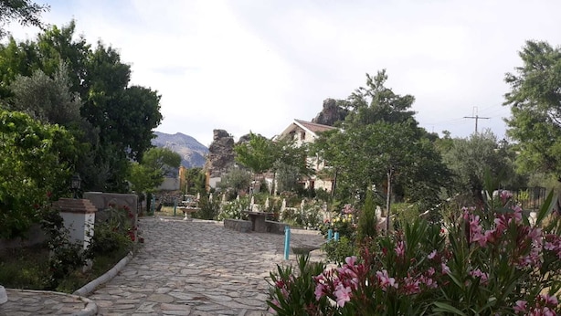 Un sendero empedrado que atraviesa un jardín con plantas en flor y árboles, rodeado de edificios de arquitectura tradicional.