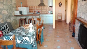 Un comedor acogedor con una mesa dispuesta para cuatro, una cocina con microondas y calentador de agua, y una chimenea al fondo.