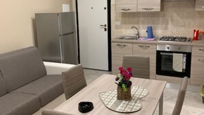 A compact living space with a kitchenette, a sofa, a dining table with chairs, and a small side table.