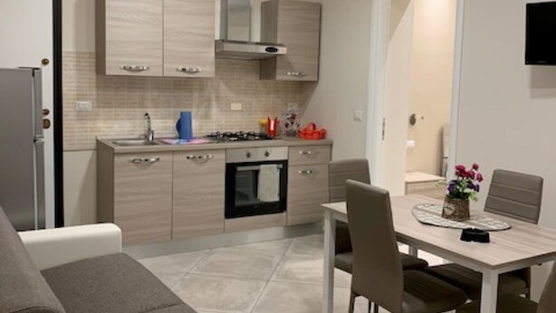 A modern kitchen with light wood cabinets, a gas stove, and a built-in oven. There is a dining table with chairs and a small decorative vase.