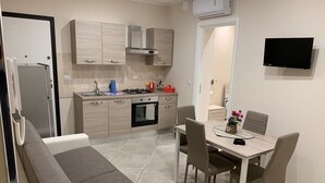 A compact kitchen with a dining area, a sofa, and a flat-screen TV.