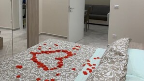 A bedroom with a bed, a mirror, a door, and a hallway leading to another room.