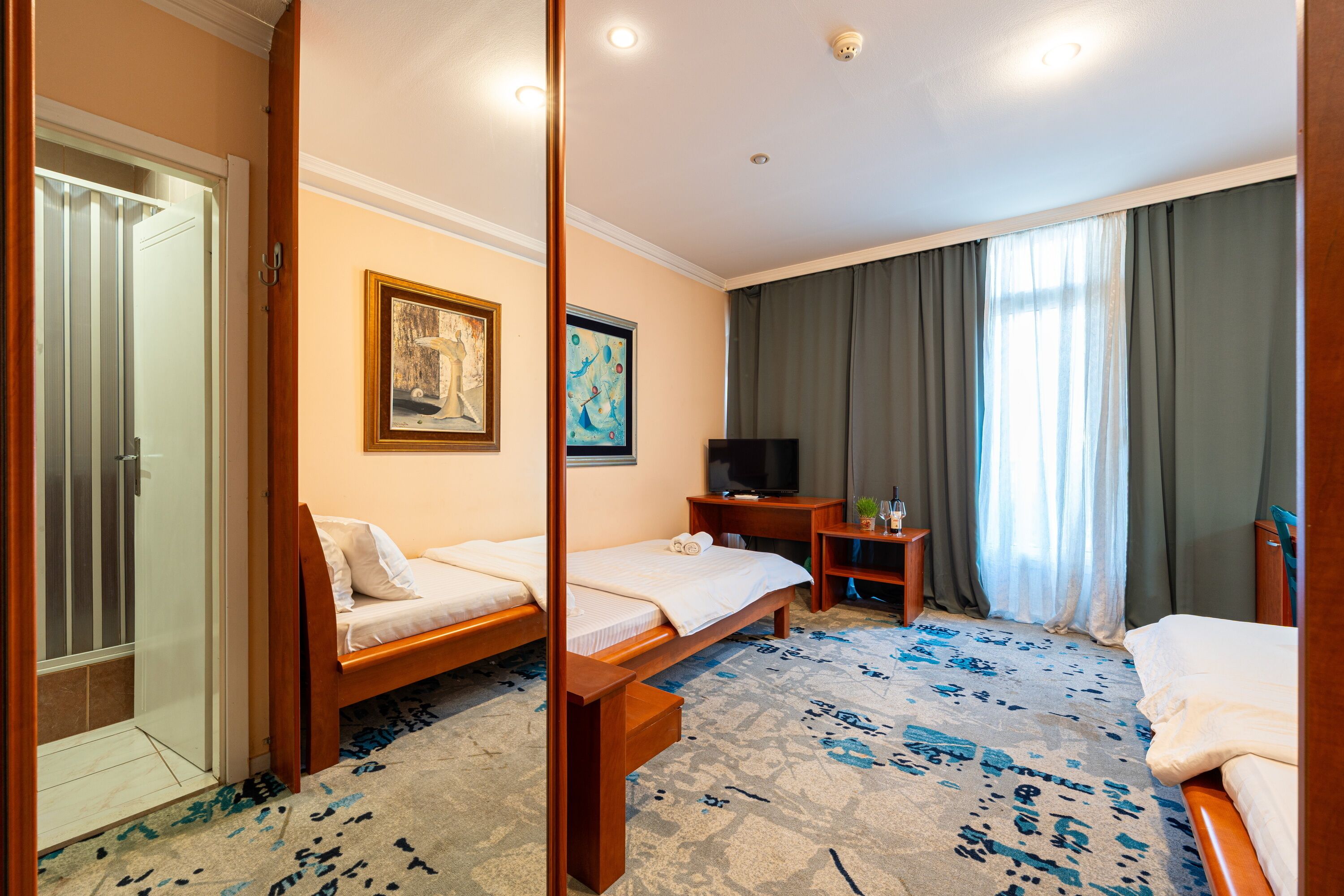 A hotel room with two beds, a television, a desk with a chair, and a window with curtains.