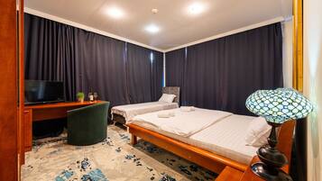 Une chambre d’hôtel avec deux lits, un bureau avec une télévision, une lampe et une moquette à motifs.