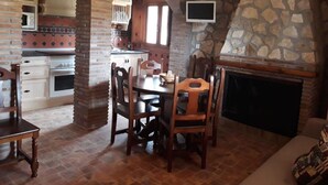 A cozy dining area with a brick fireplace, stone walls, and a television mounted above it. - Casita Vista Alegre. (castril)