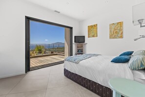 A bedroom with a large bed, a TV, artwork, and a balcony with a view.