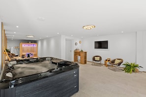 A modern living room with a large black hot tub, a wooden bar area, and a flat-screen TV mounted on the wall.