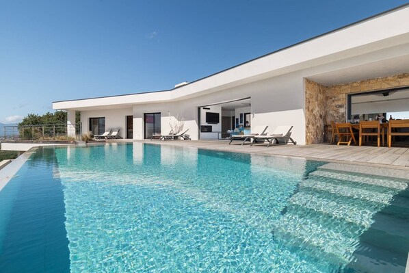 A modern poolside area with a clear pool, lounge chairs, and a stone wall.