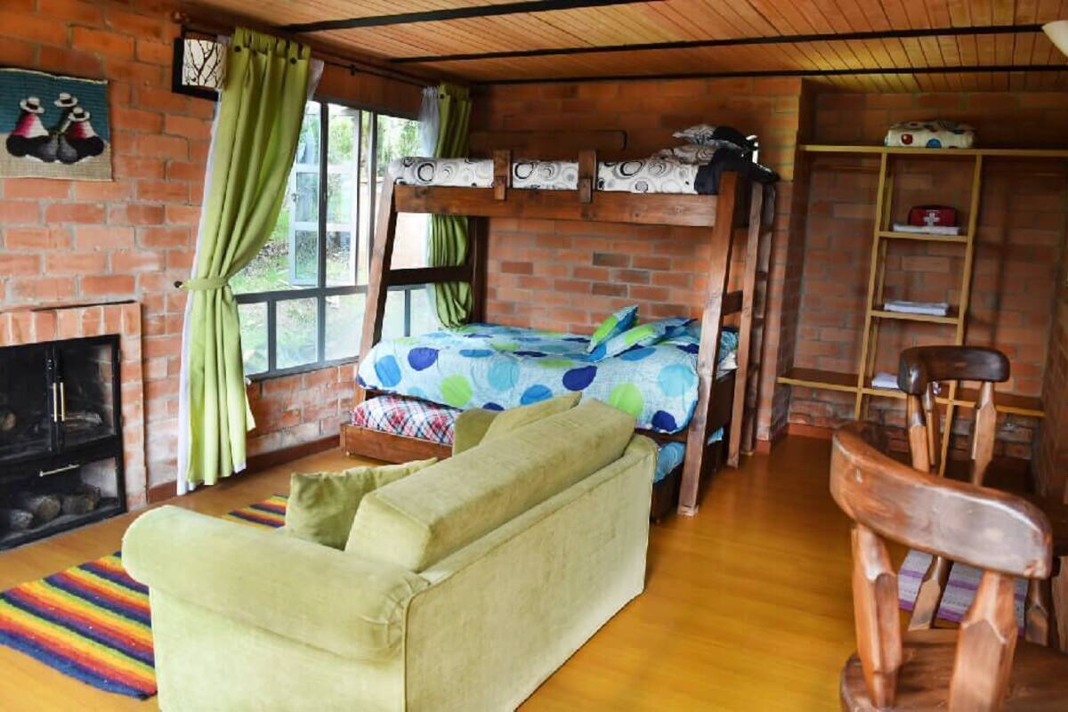 A rustic room with a bunk bed, a sofa, a wooden chair, a fireplace, and a window with curtains.