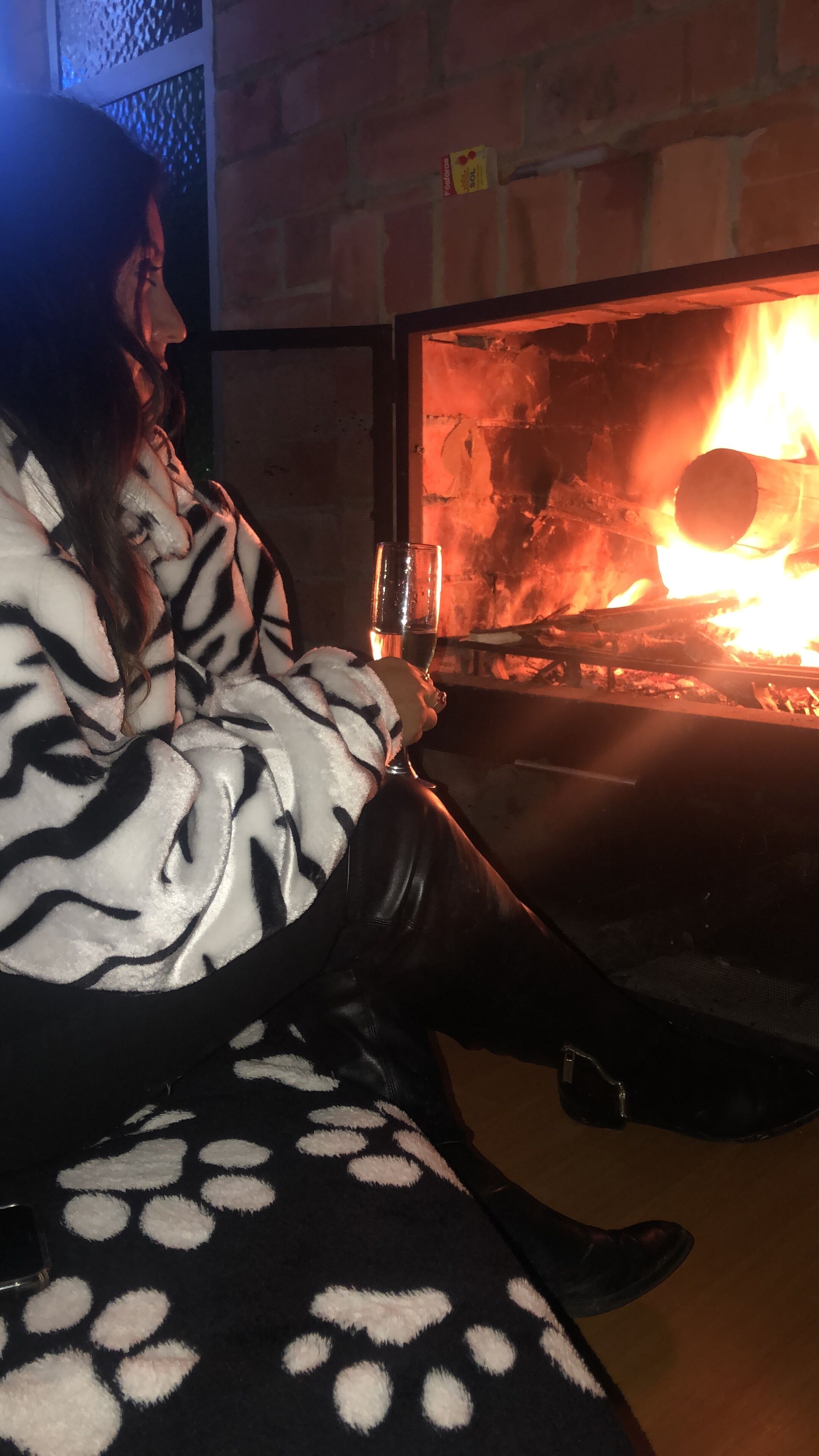 A person sitting by a fireplace with a glass of water.