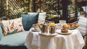 Une table dressée pour le petit-déjeuner, avec une théière, des tasses et des viennoiseries, et une vue sur la verdure à travers une fenêtre à treillis.