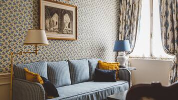 Una habitación con papel tapiz estampado, un sofá con cojines, un cuadro en la pared y una ventana con cortinas.