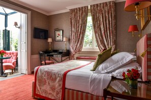 A bedroom with a bed, a desk, a chair, and a window with curtains.