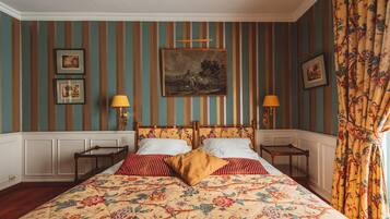 Una cama con una colcha estampada, almohadas a rayas y un cabecero de madera. Hay dos mesitas de noche con lámparas.
